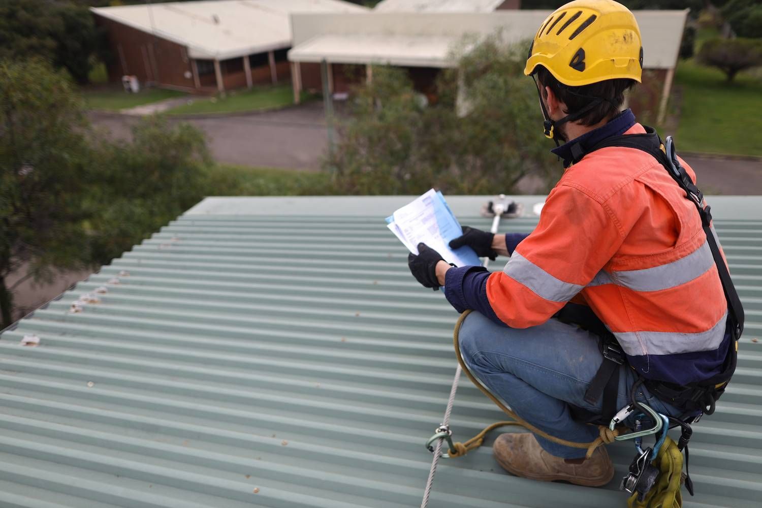 A Man is Kneeling on a Roof Looking at a Piece of Paper — Ron Nickel Roofing in Gold Coast, QLD