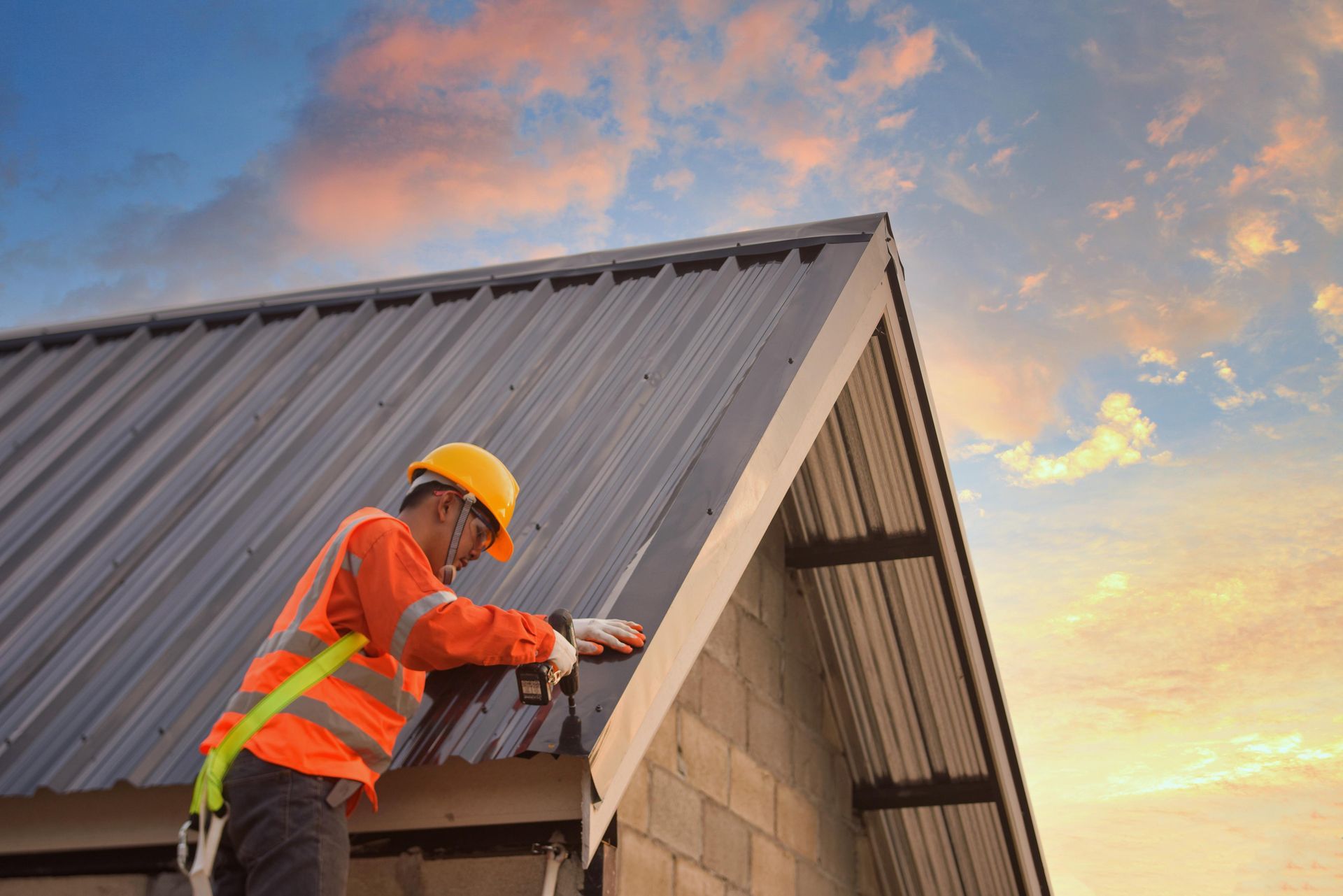 Roofer Wearing Safety Gear Working On A Metal Roof Against A Sunset Sky