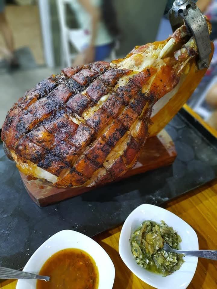 Un jamón asado con una corteza crujiente y marcada, servido sobre una tabla de madera y acompañado de pequeños cuencos
