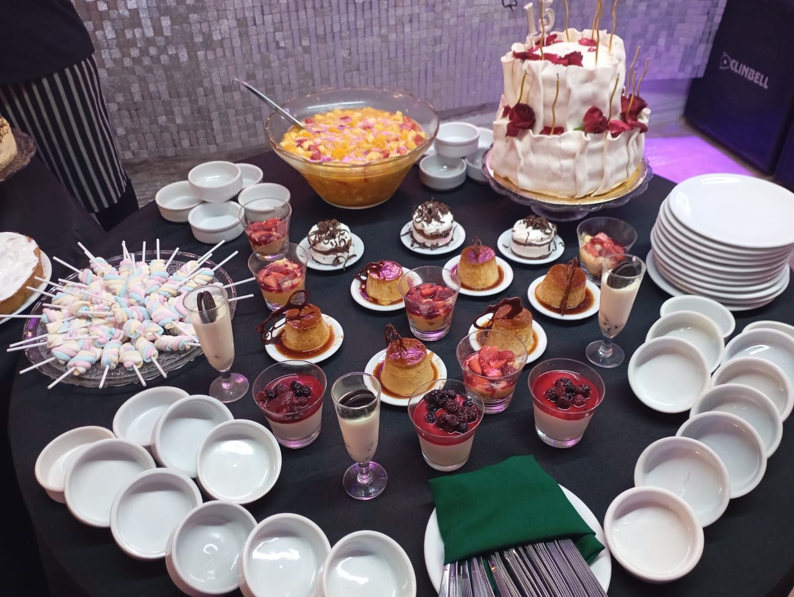 Una mesa de banquete con un pastel de dos pisos, un frutero, una variedad de pequeños postres