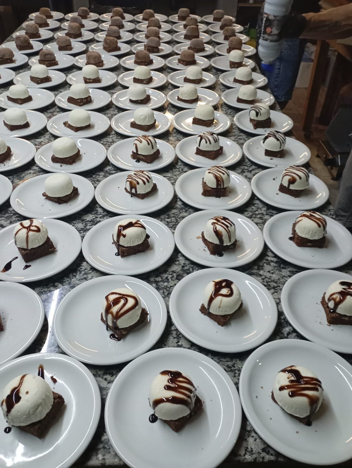 Filas de pequeños postres con cobertura blanca, elaborados con cuadrados de brownie y bañados en chocolate
