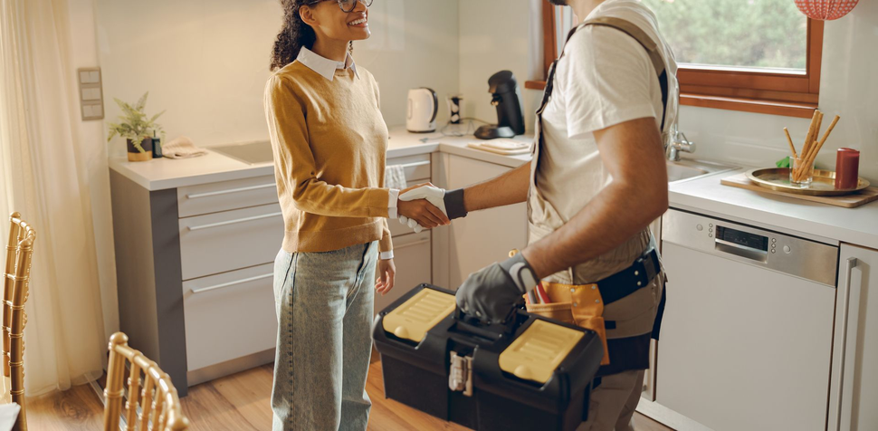 Woman and a worker shaking hands in a kitchen, a toolbox on the floor.