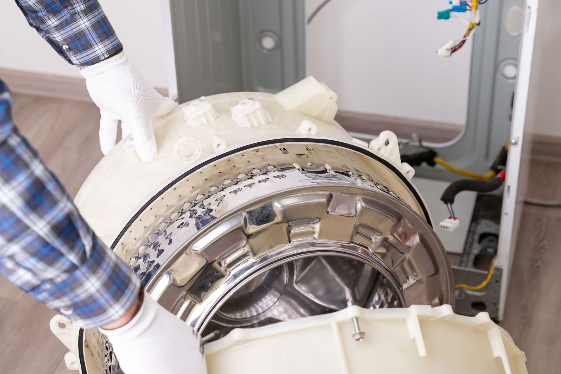 Hands in white gloves repairing the disassembled drum of a washing machine.