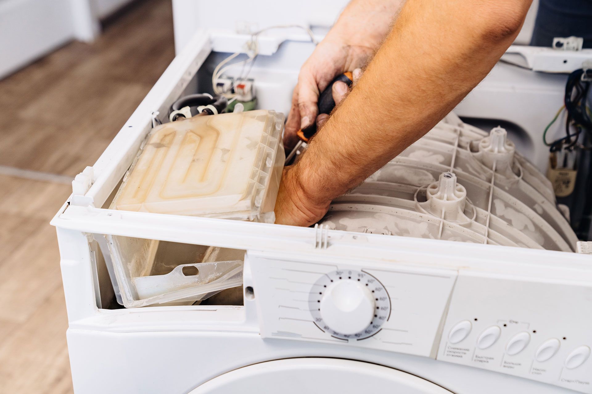 Person repairs a washing machine, using a screwdriver to work inside the open machine.