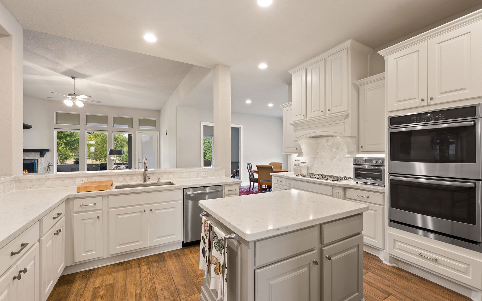 Bright white kitchen with a gray island, stainless steel appliances, and hardwood floors.