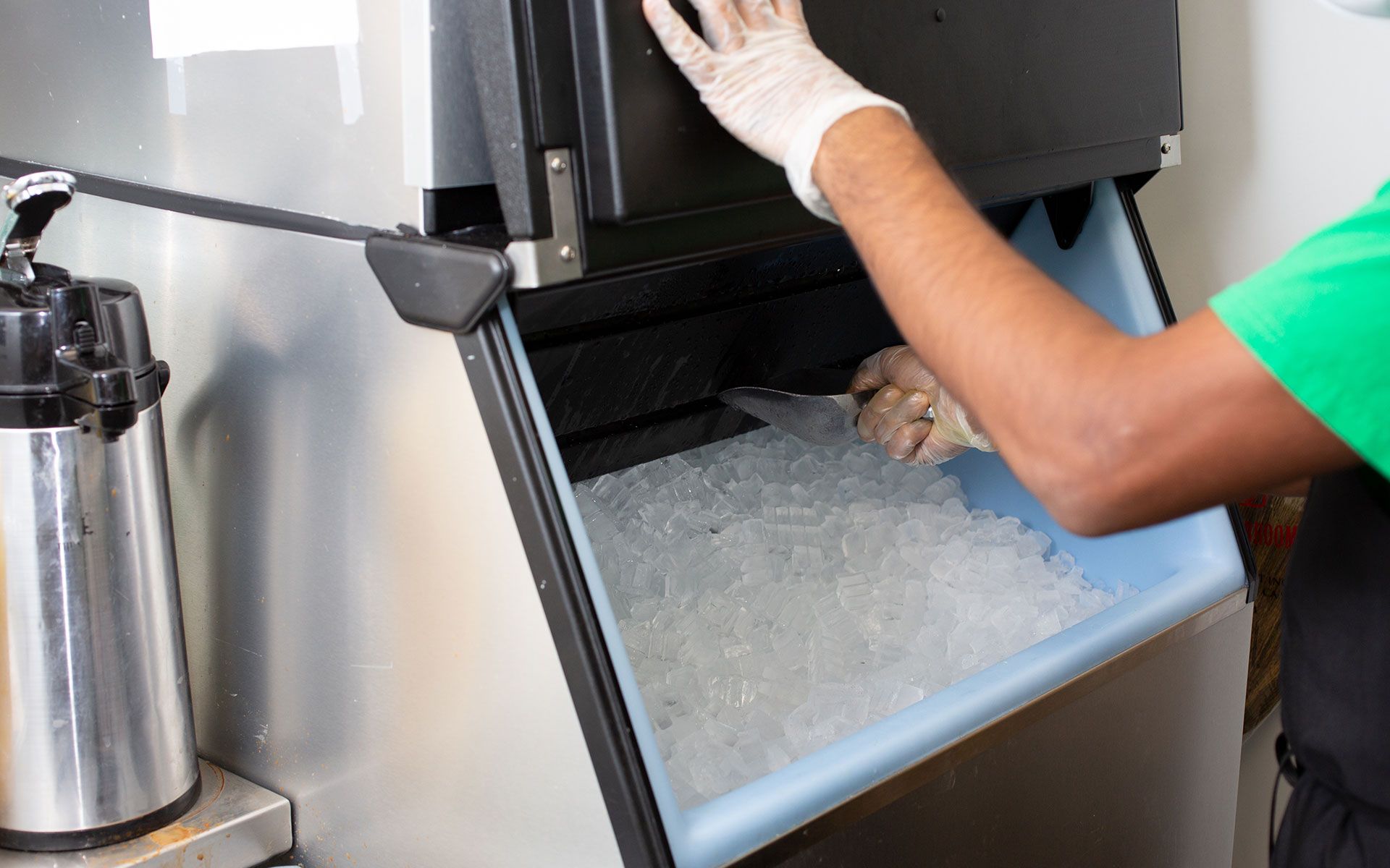 Person in gloves scooping ice from an ice machine's bin.