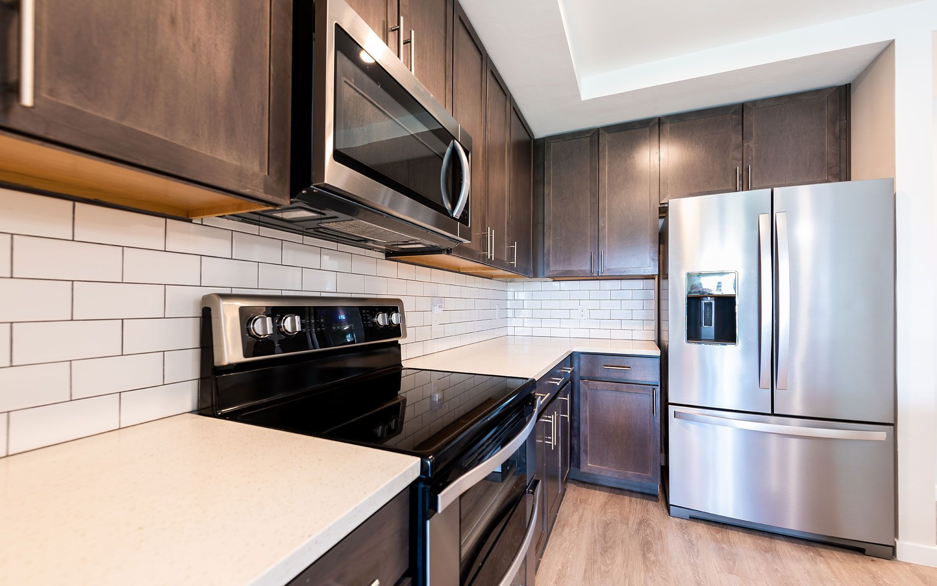 Kitchen with dark brown cabinets, stainless steel appliances, white subway tile backsplash, and light countertops.