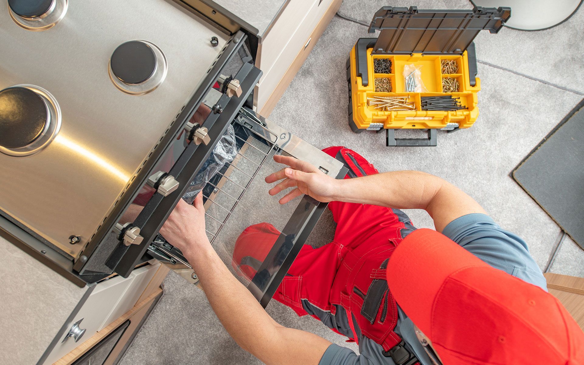 Person repairing a kitchen oven, with a toolbox nearby.