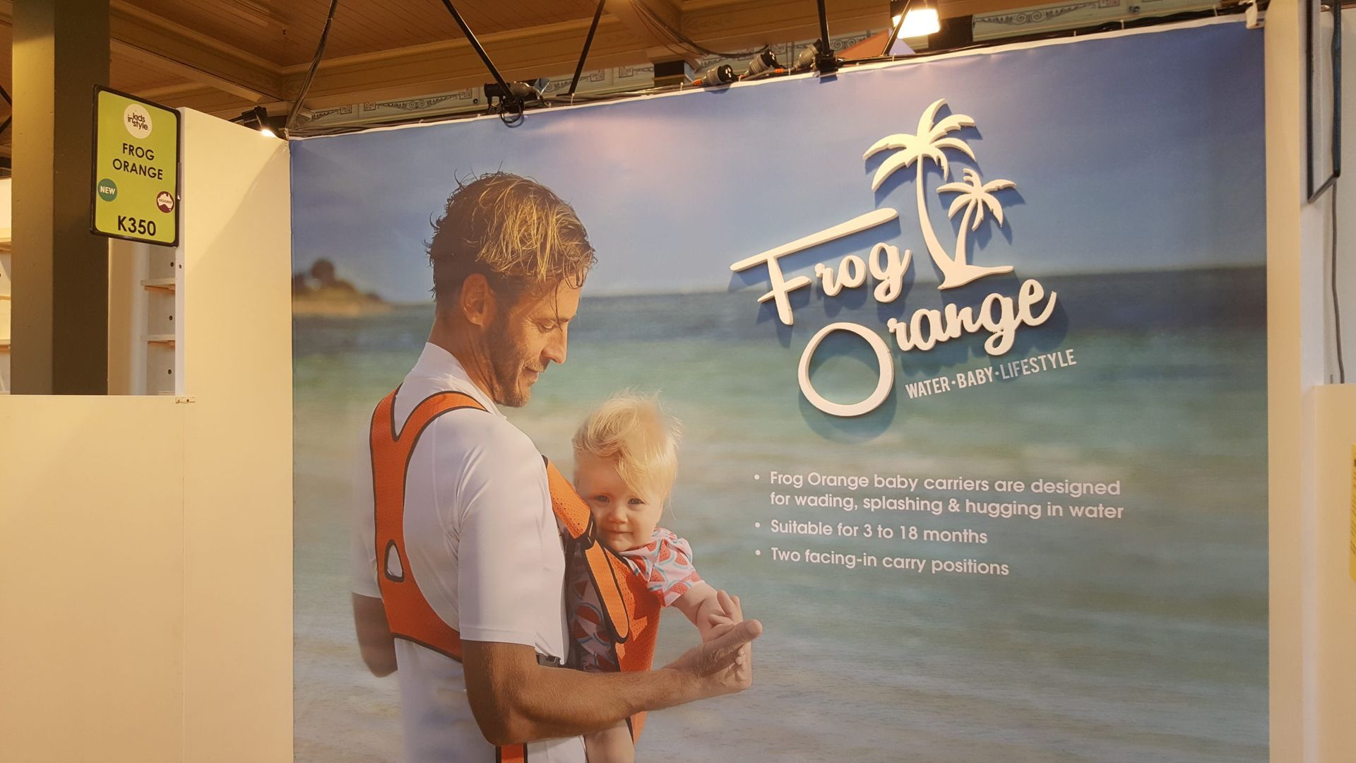 A man is holding a baby in a frog orange carrier.