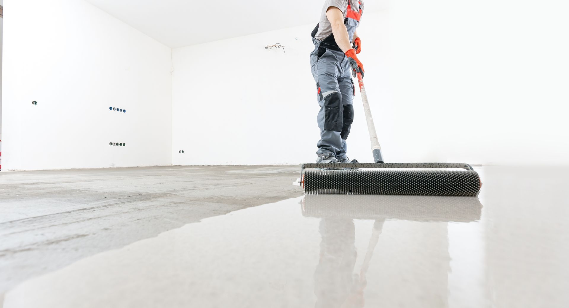 A man is cleaning a concrete floor with a broom.