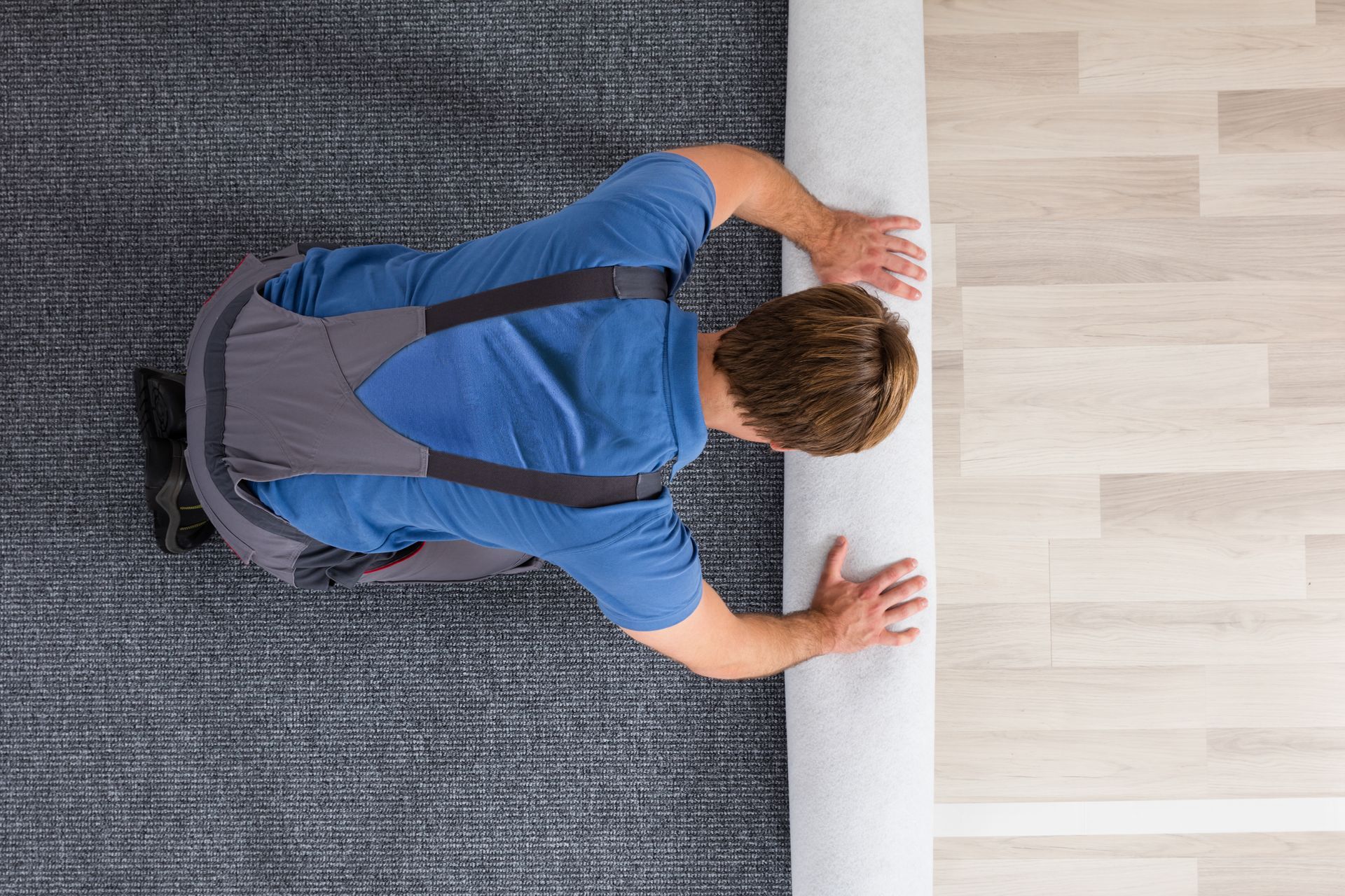 A man is rolling a carpet on the floor.