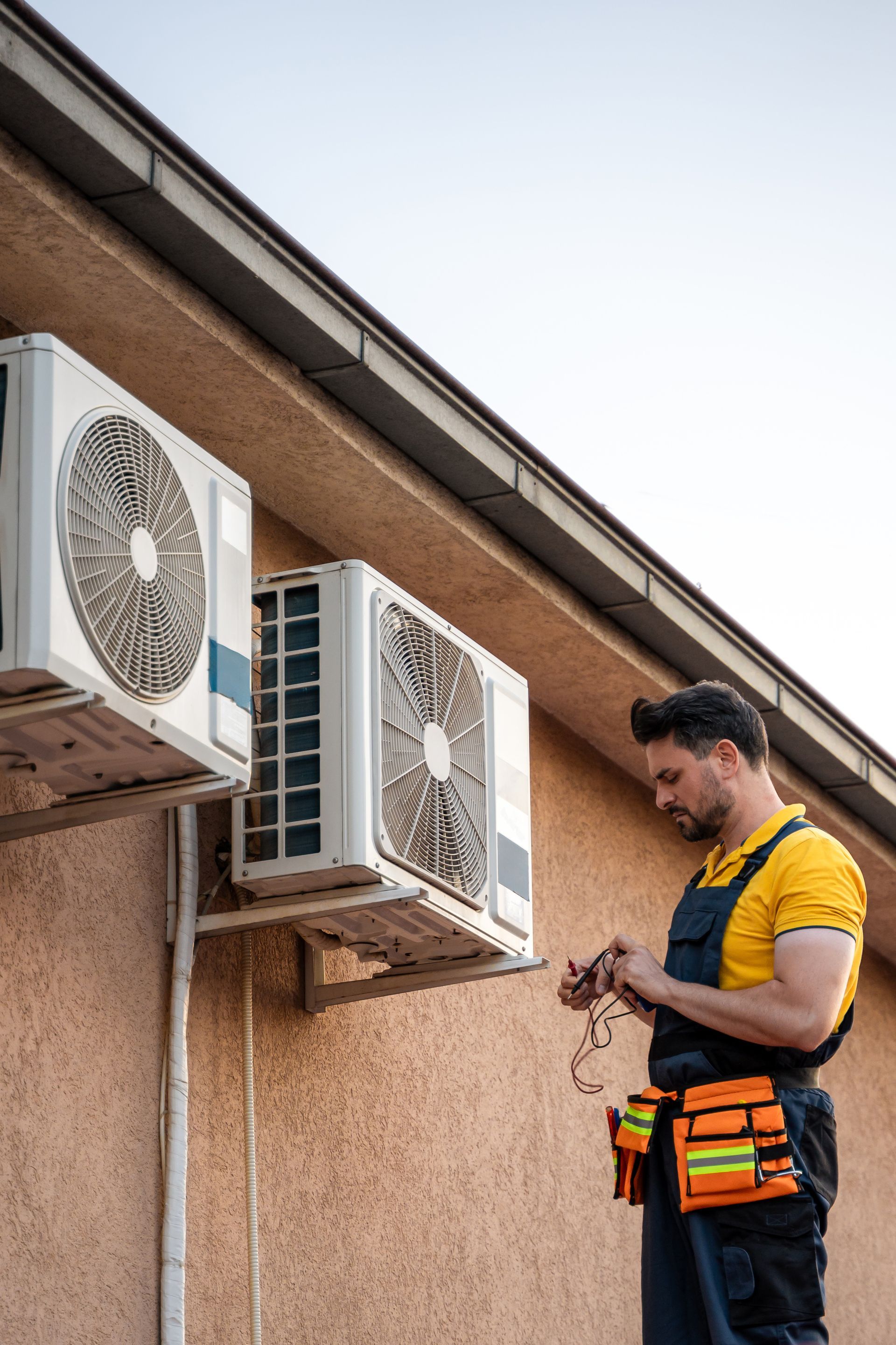 An HVAC technician performs maintenance on air conditioning units at a residential building