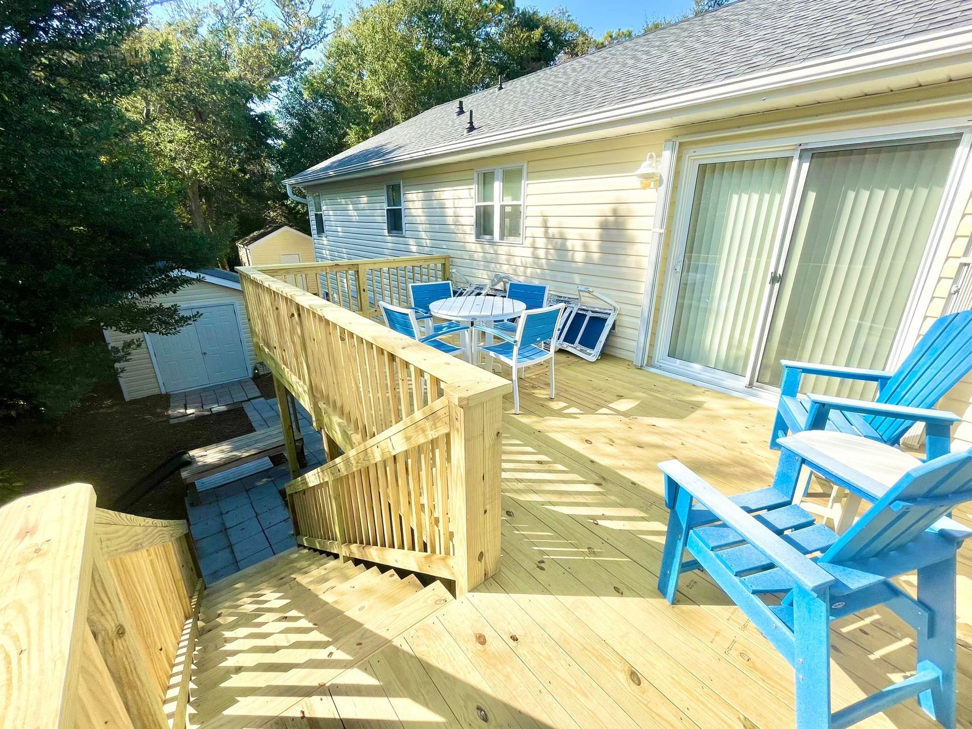 A wooden deck with blue chairs and a table in front of a house.