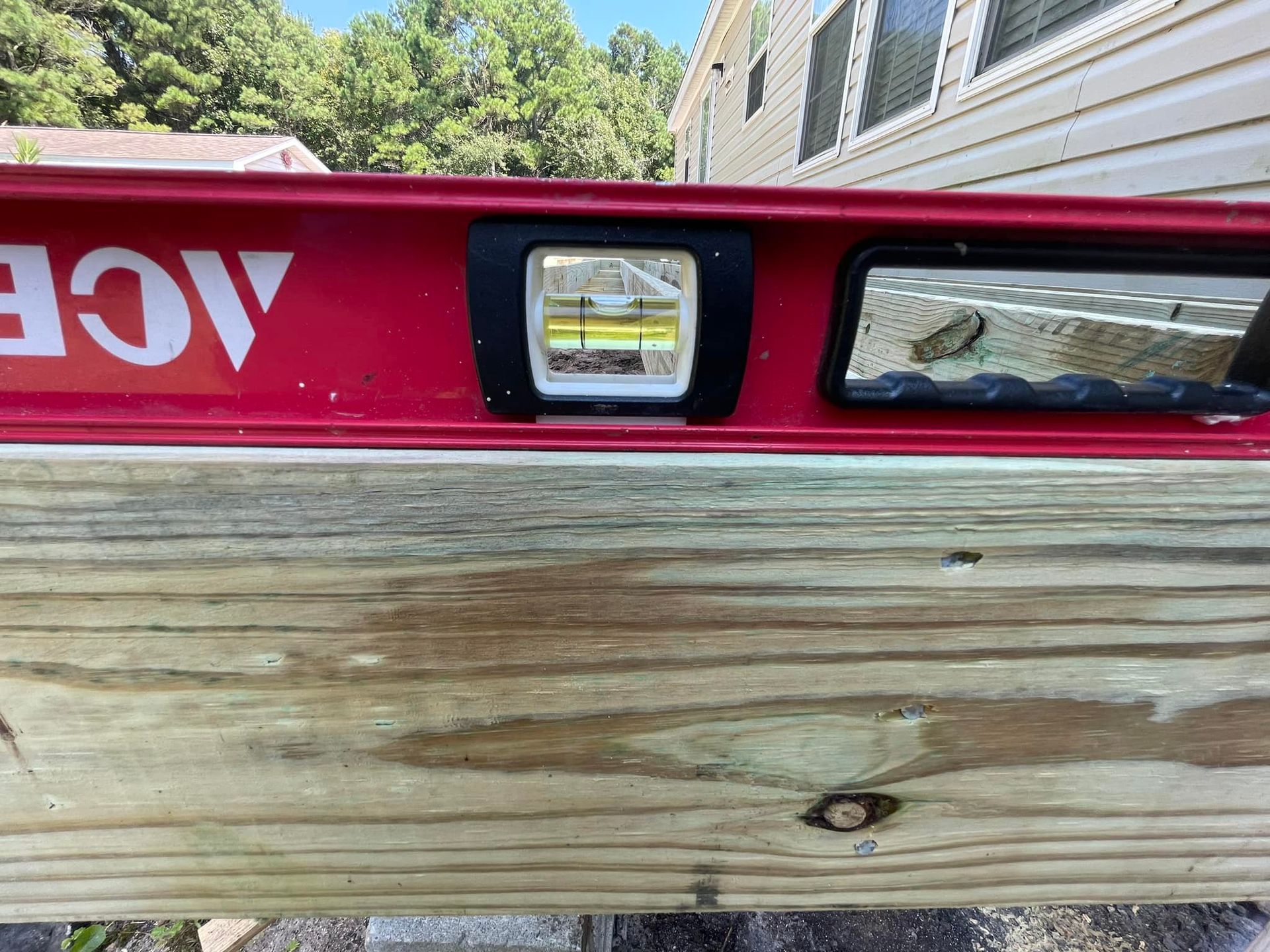 A red level is sitting on top of a piece of wood.