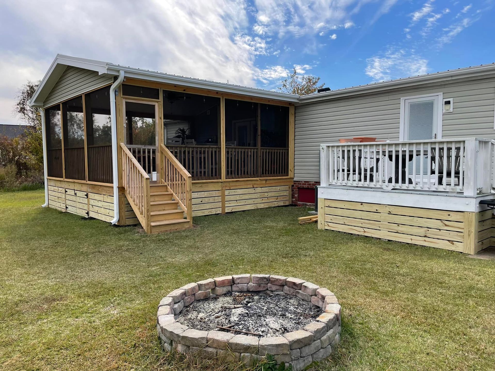 A mobile home with a screened in porch and a fire pit in front of it.