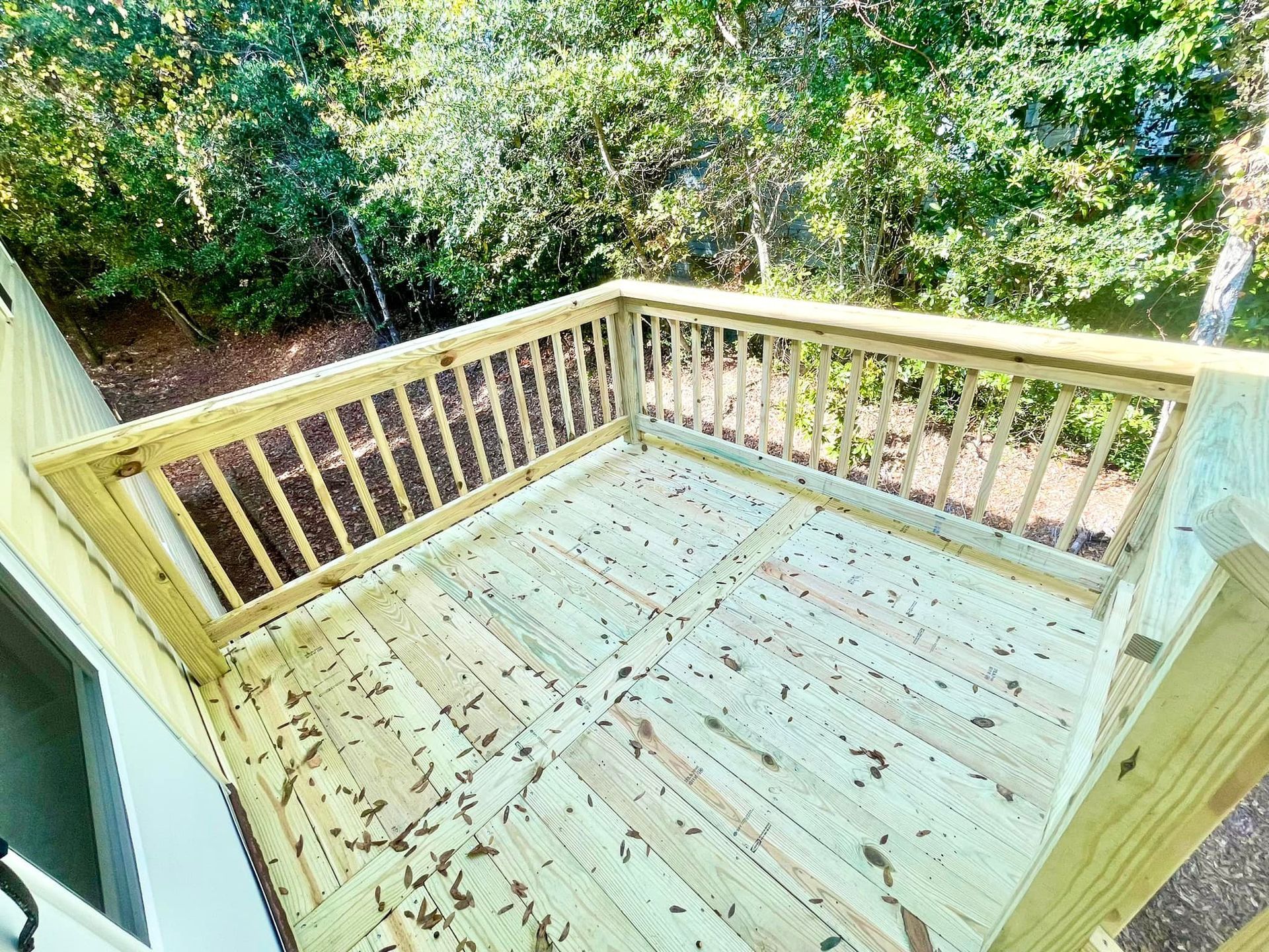 A wooden deck with a railing and trees in the background.
