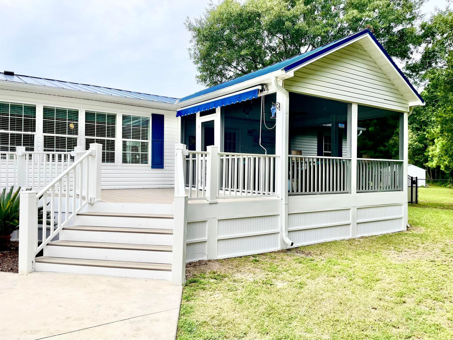 A white mobile home with a blue roof and a screened in porch.