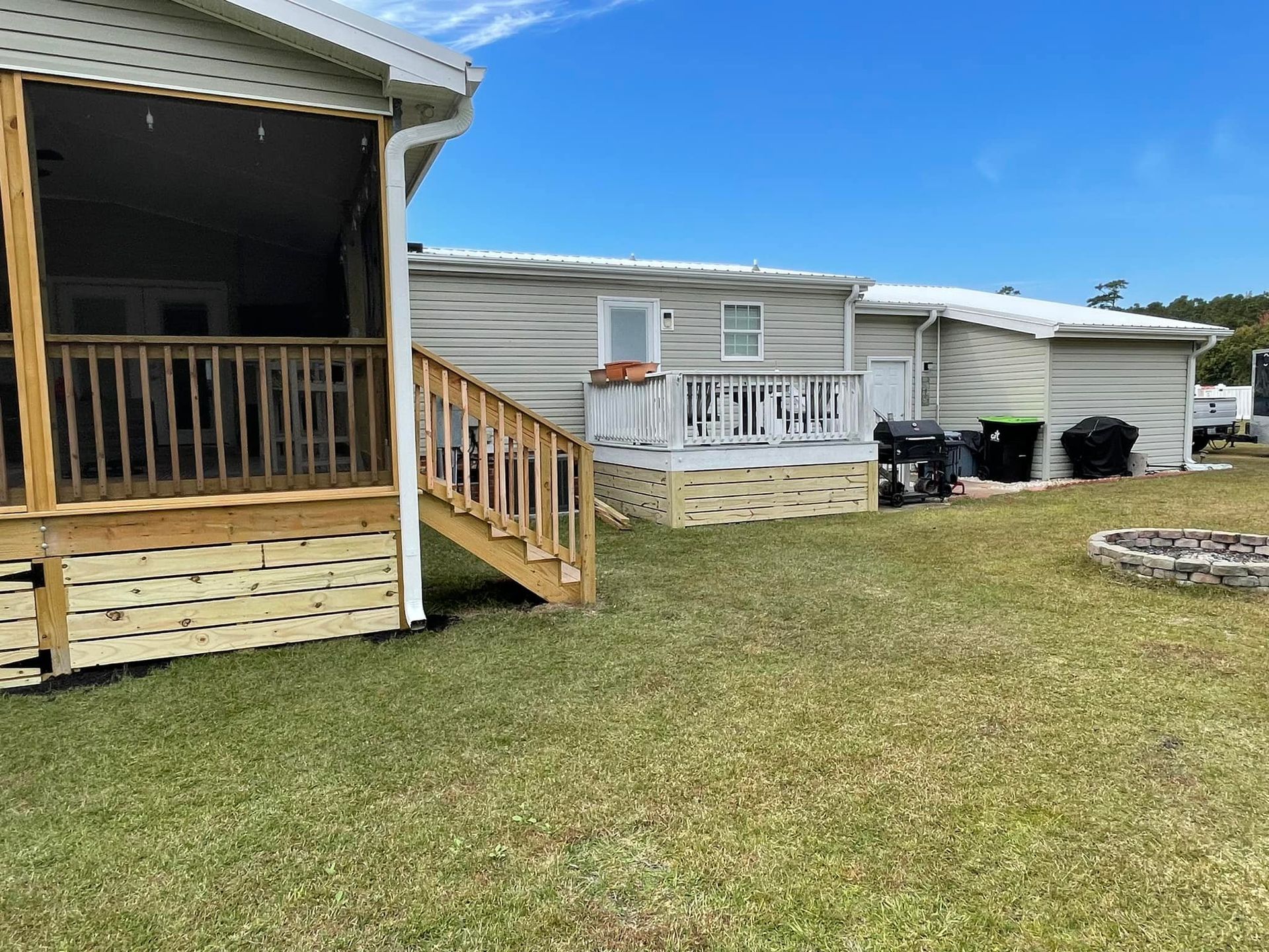 A mobile home with a screened in porch and a fire pit in the backyard.