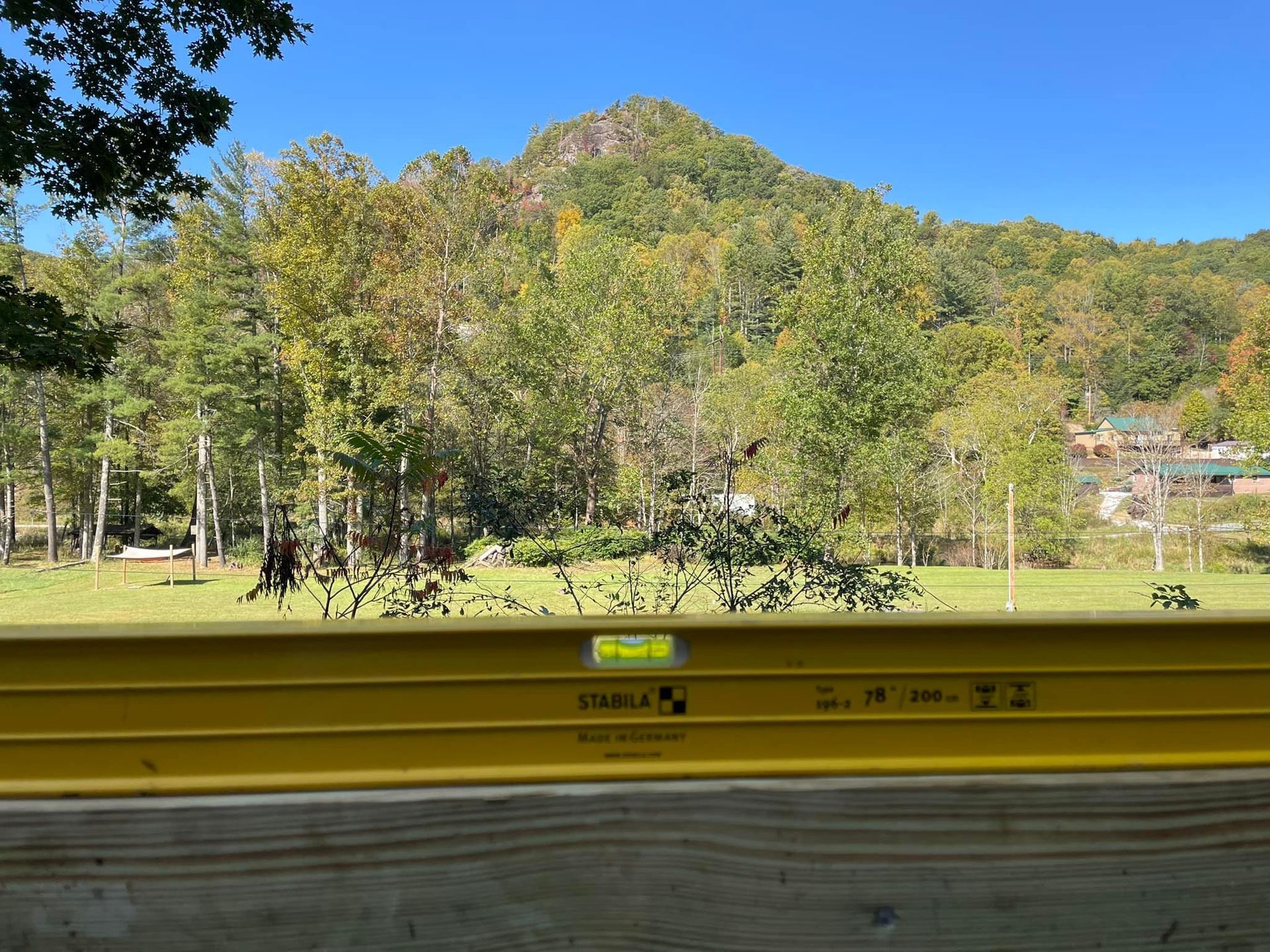 A yellow level is sitting on a wooden fence in front of a mountain.
