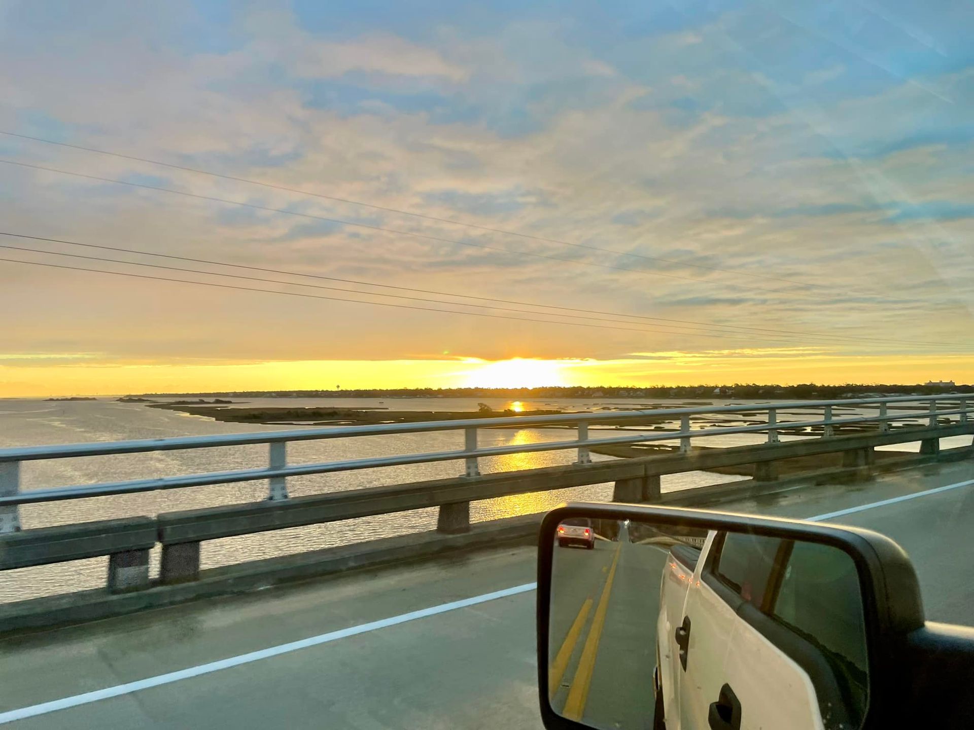A car is driving on a bridge over a body of water at sunset.