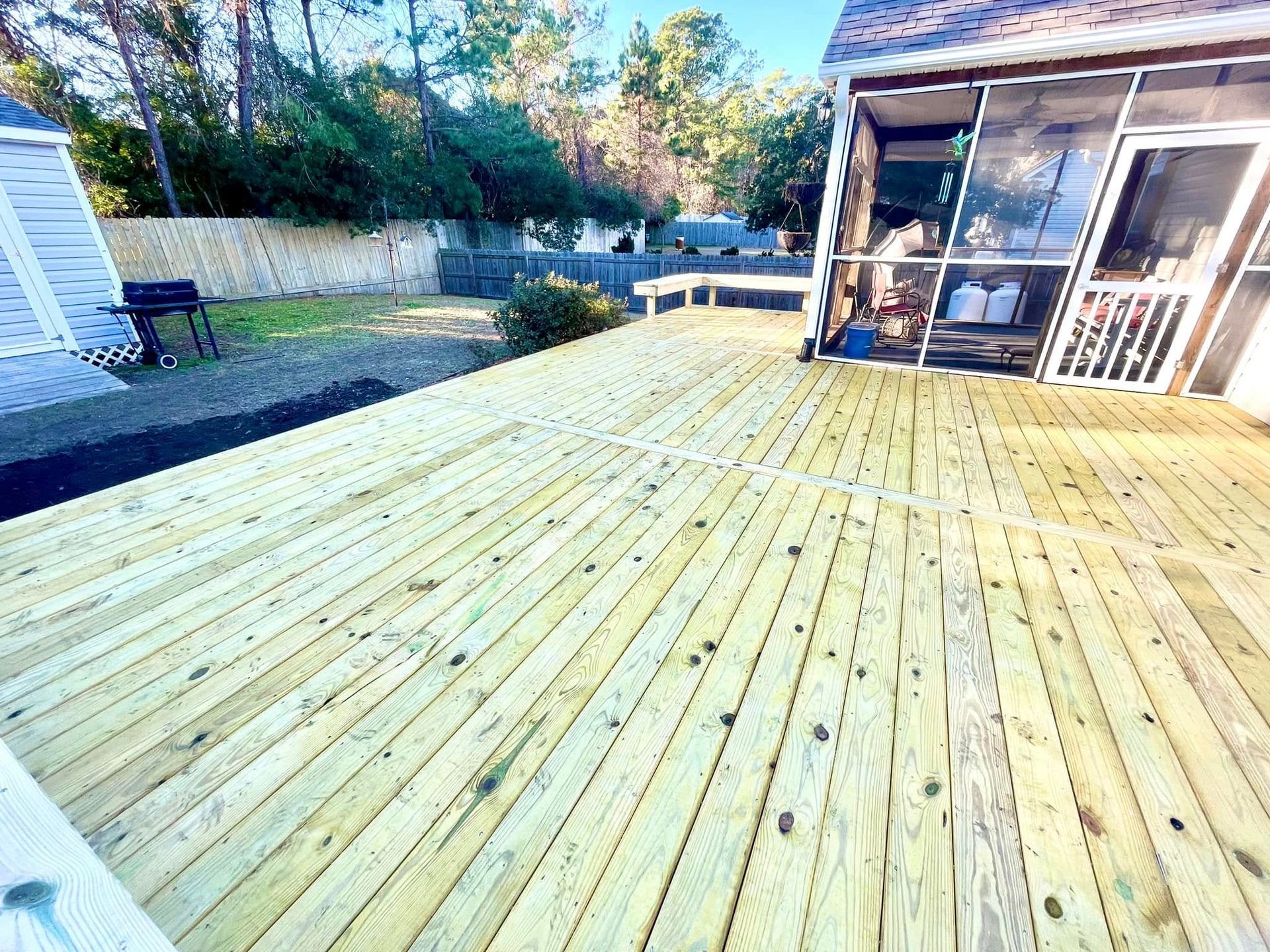 A large wooden deck with a screened in porch in the backyard of a house.