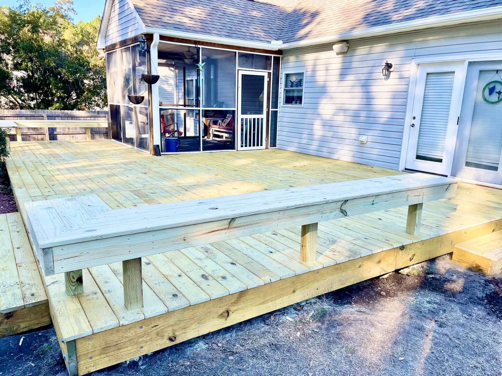 A wooden deck is sitting in front of a house with a screened in porch.
