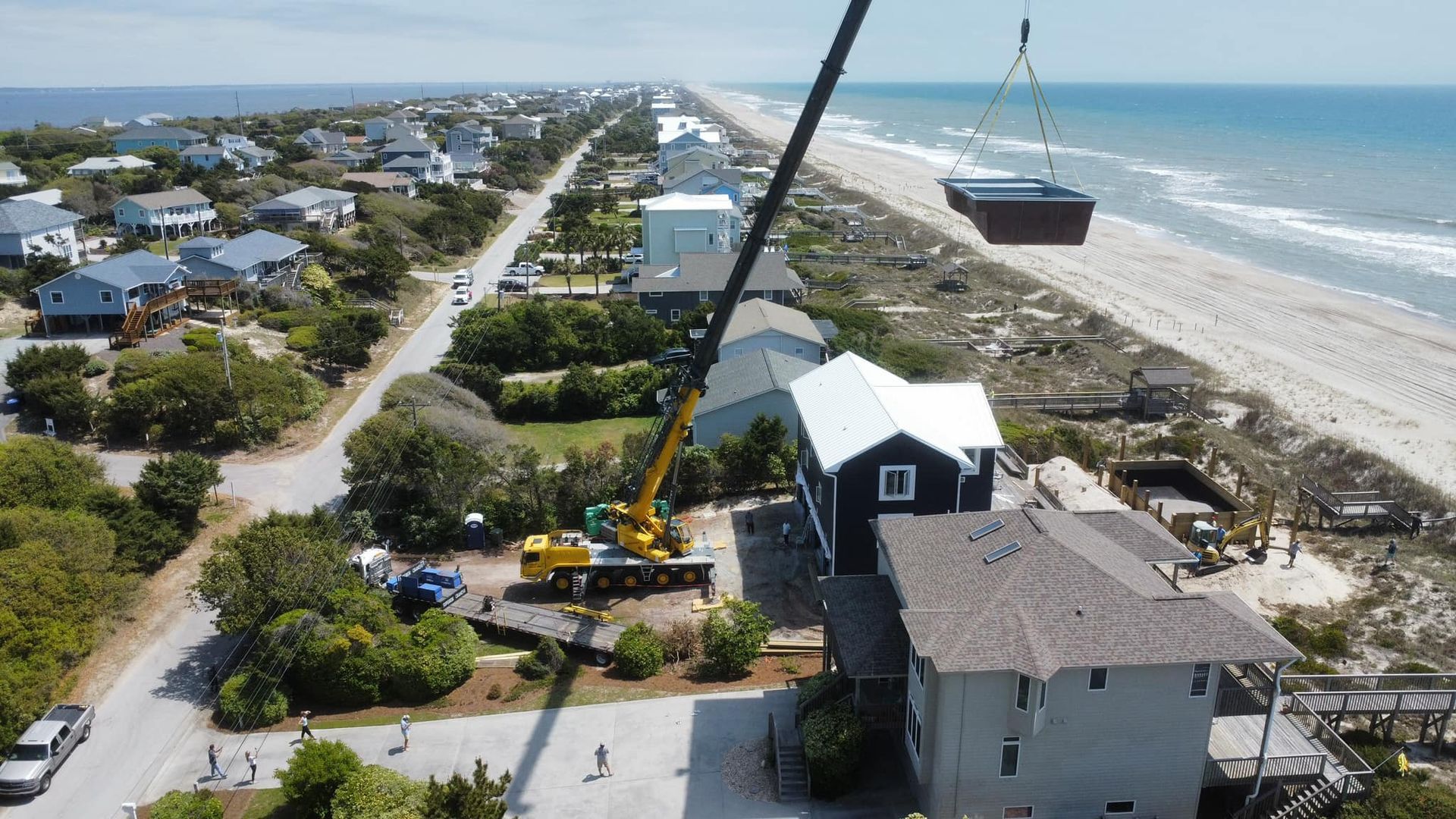 An aerial view of a house being lifted into the ocean by a crane.