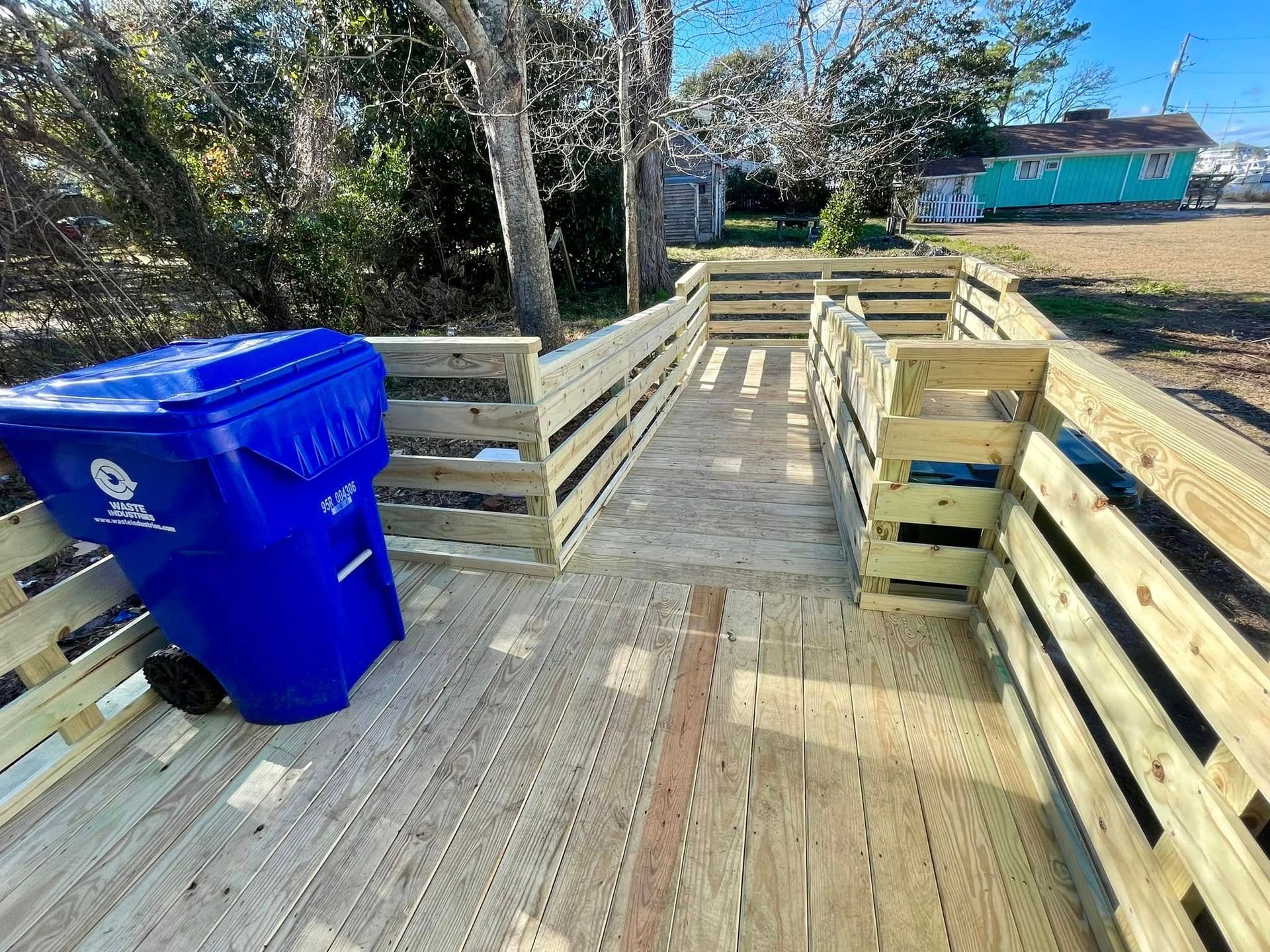 A blue trash can is sitting on top of a wooden deck.