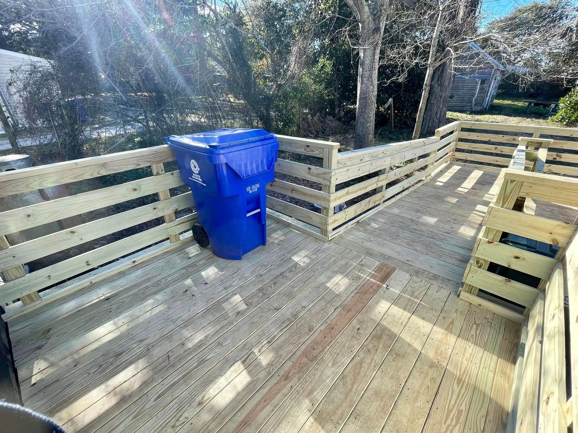 A blue trash can is sitting on a wooden deck.