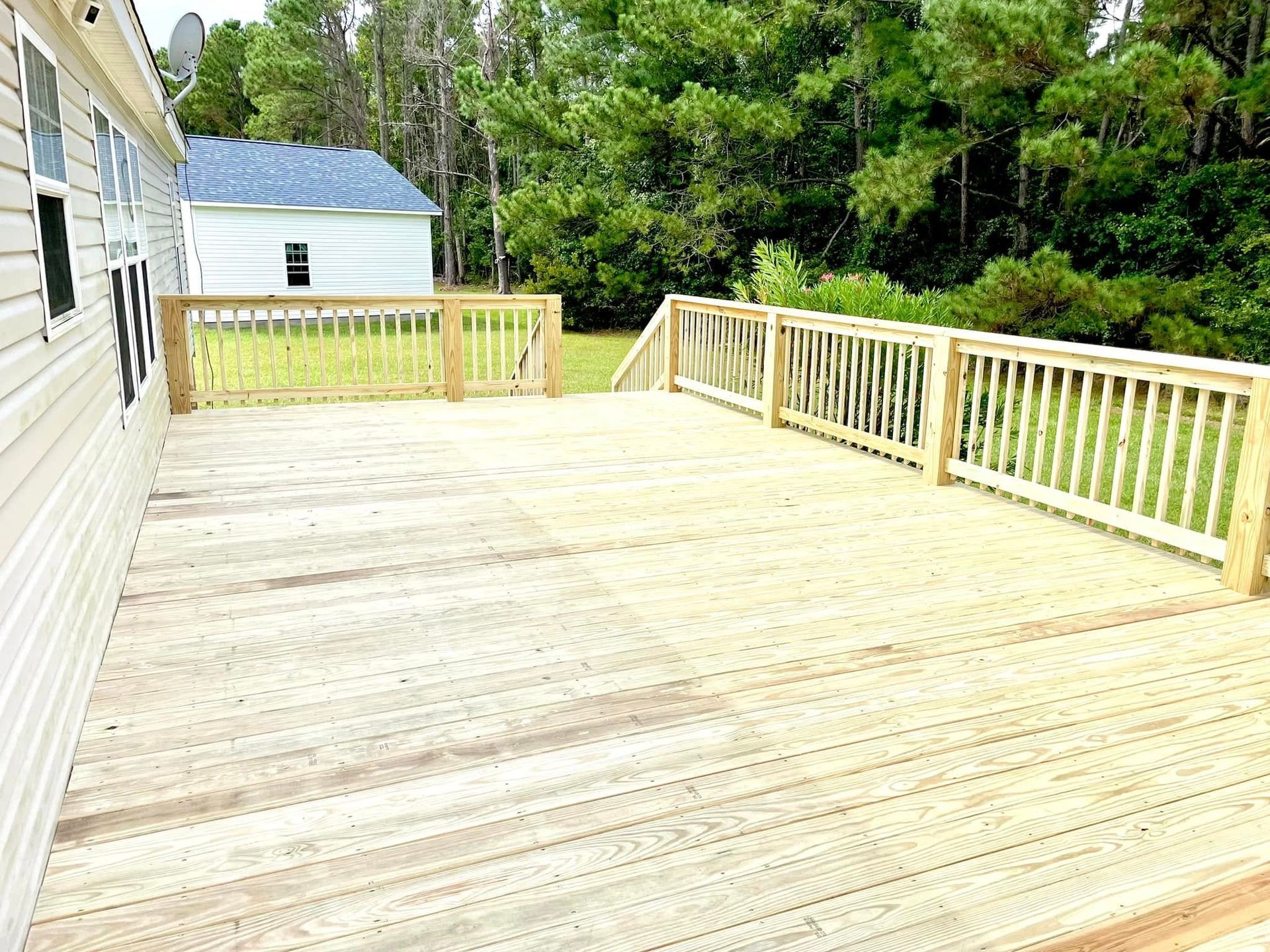 A large wooden deck with a wooden railing in front of a house.