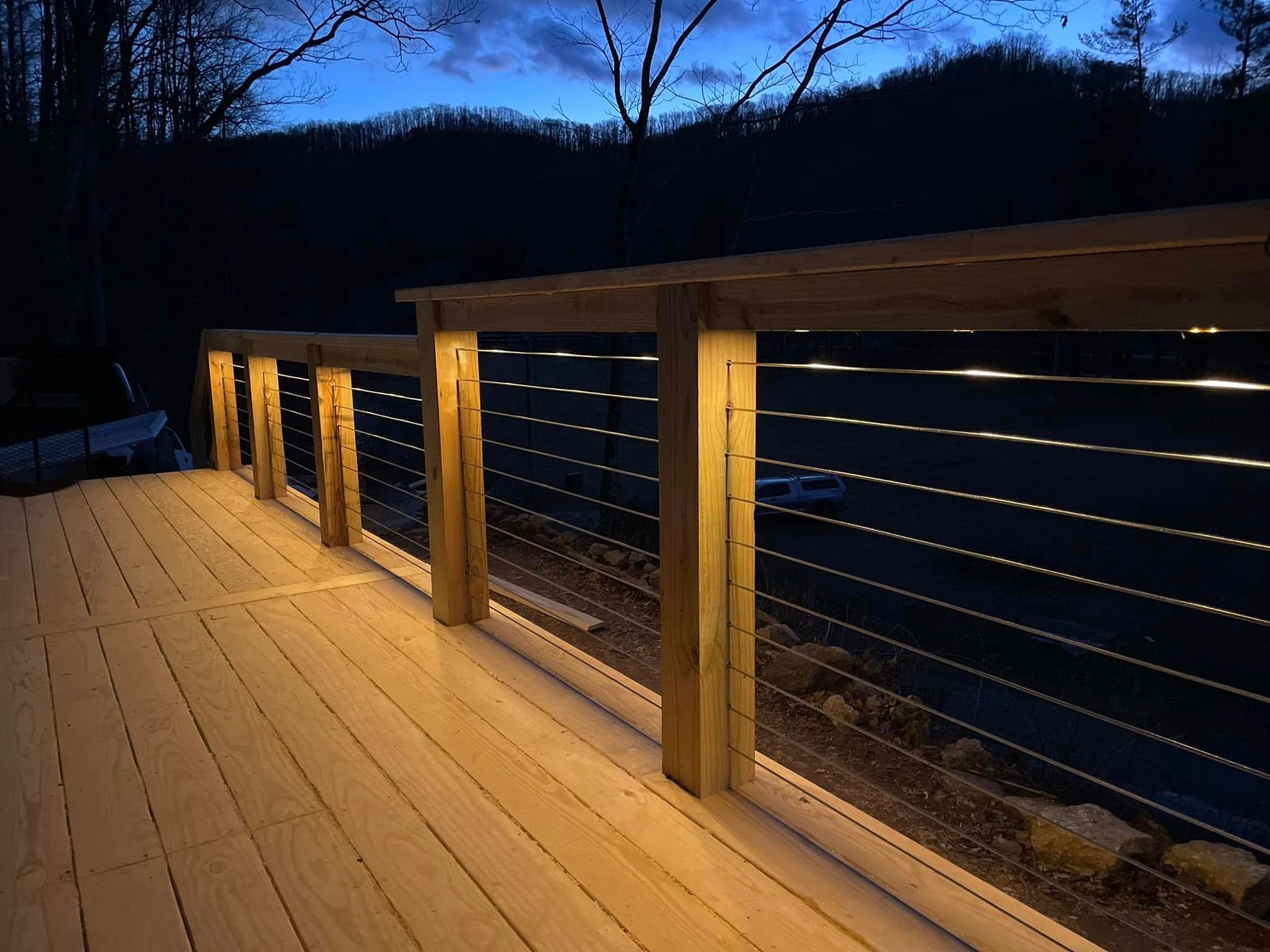 A wooden deck with a stainless steel railing is lit up at night.