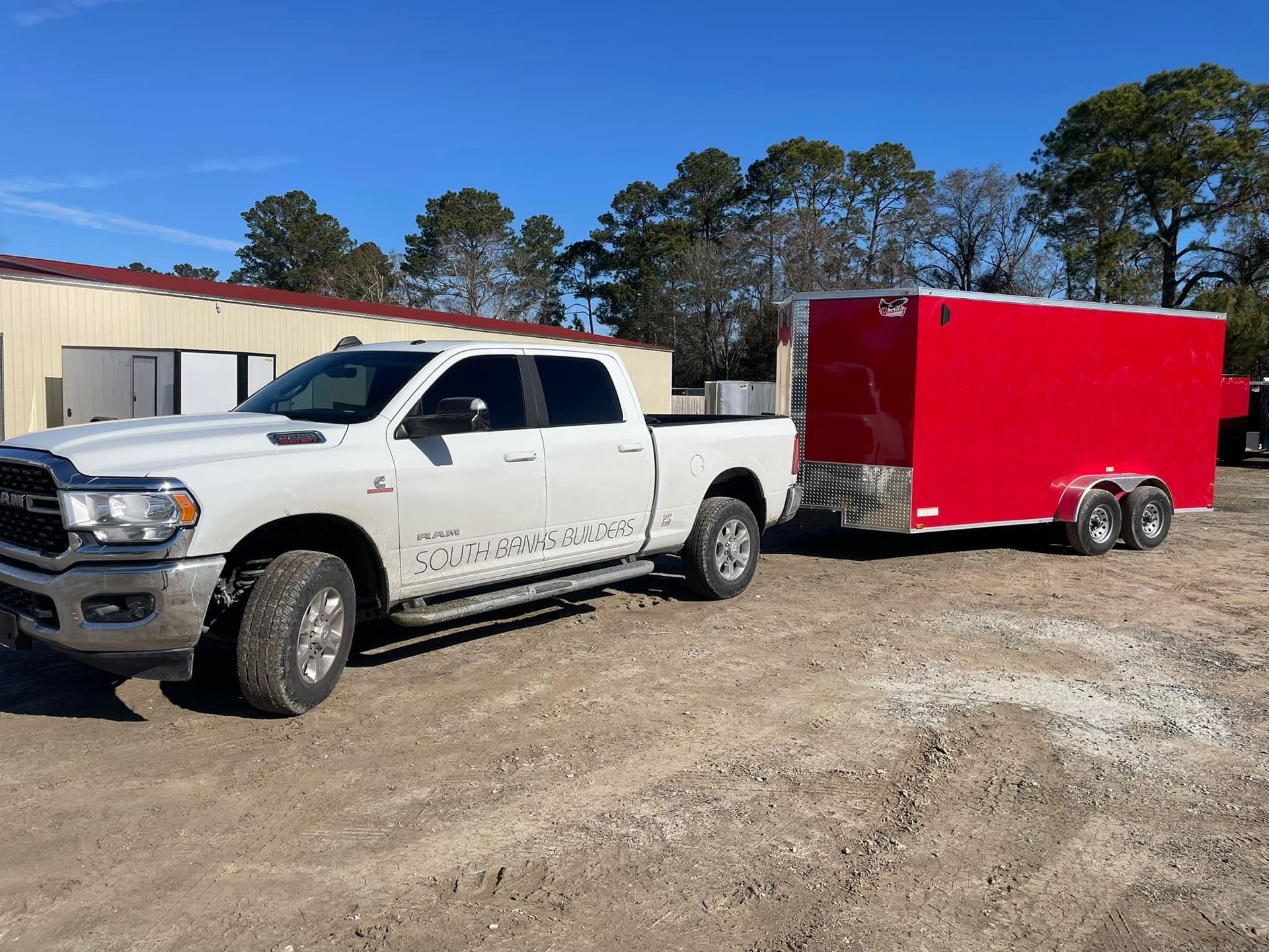 A white truck is towing a red trailer in a dirt field.
