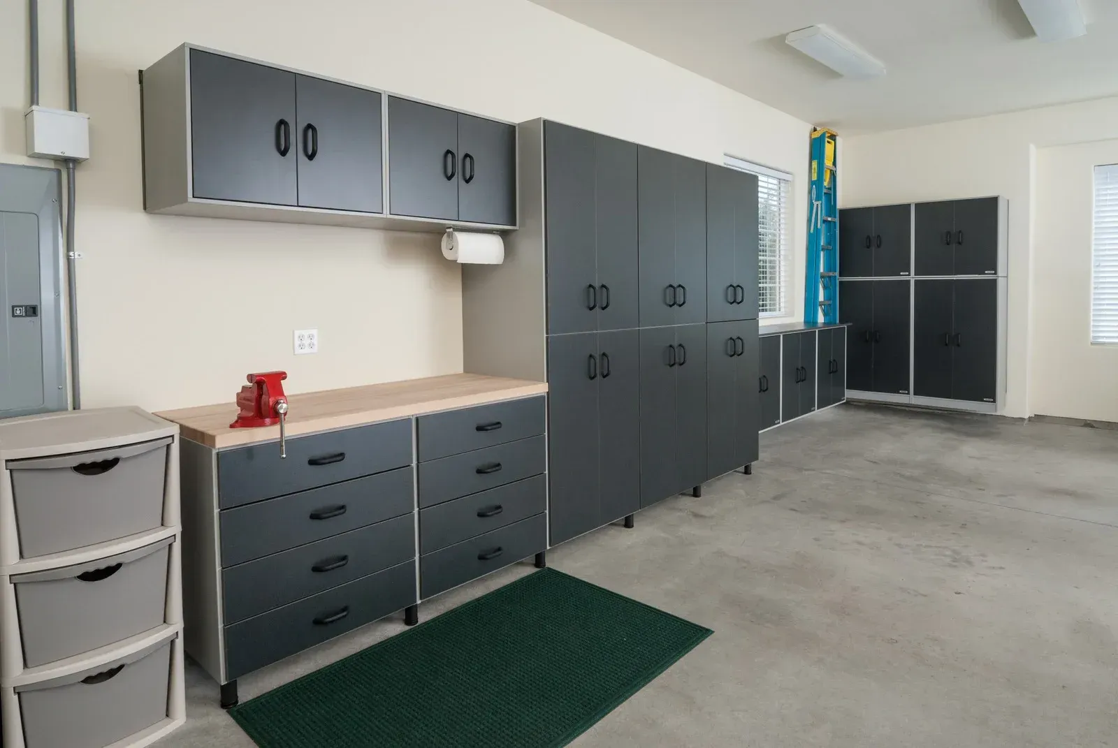 A garage with lots of cabinets and drawers and a green rug.