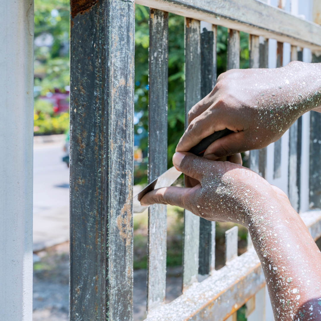 A person is sanding a metal fence with a sander.