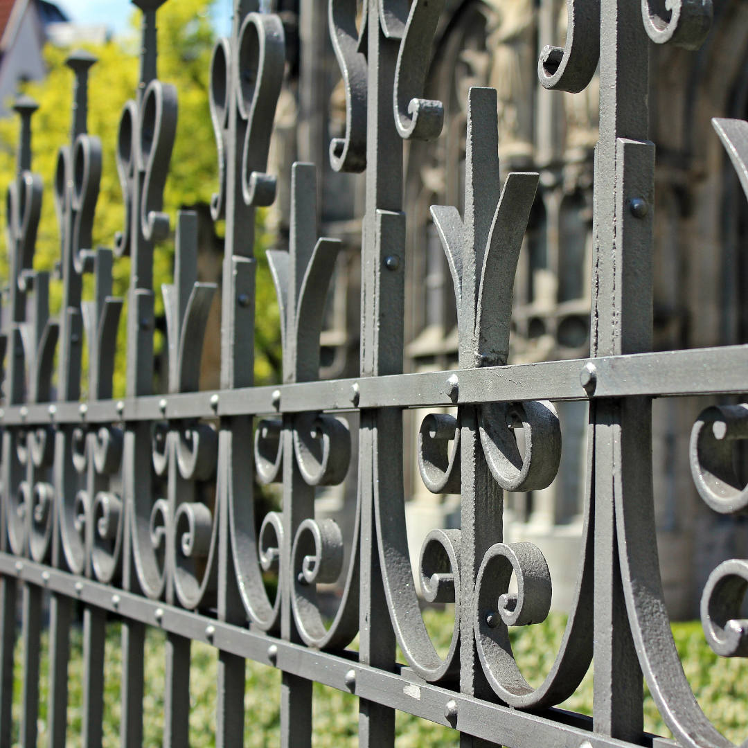 A close up of a wrought iron fence with a building in the background