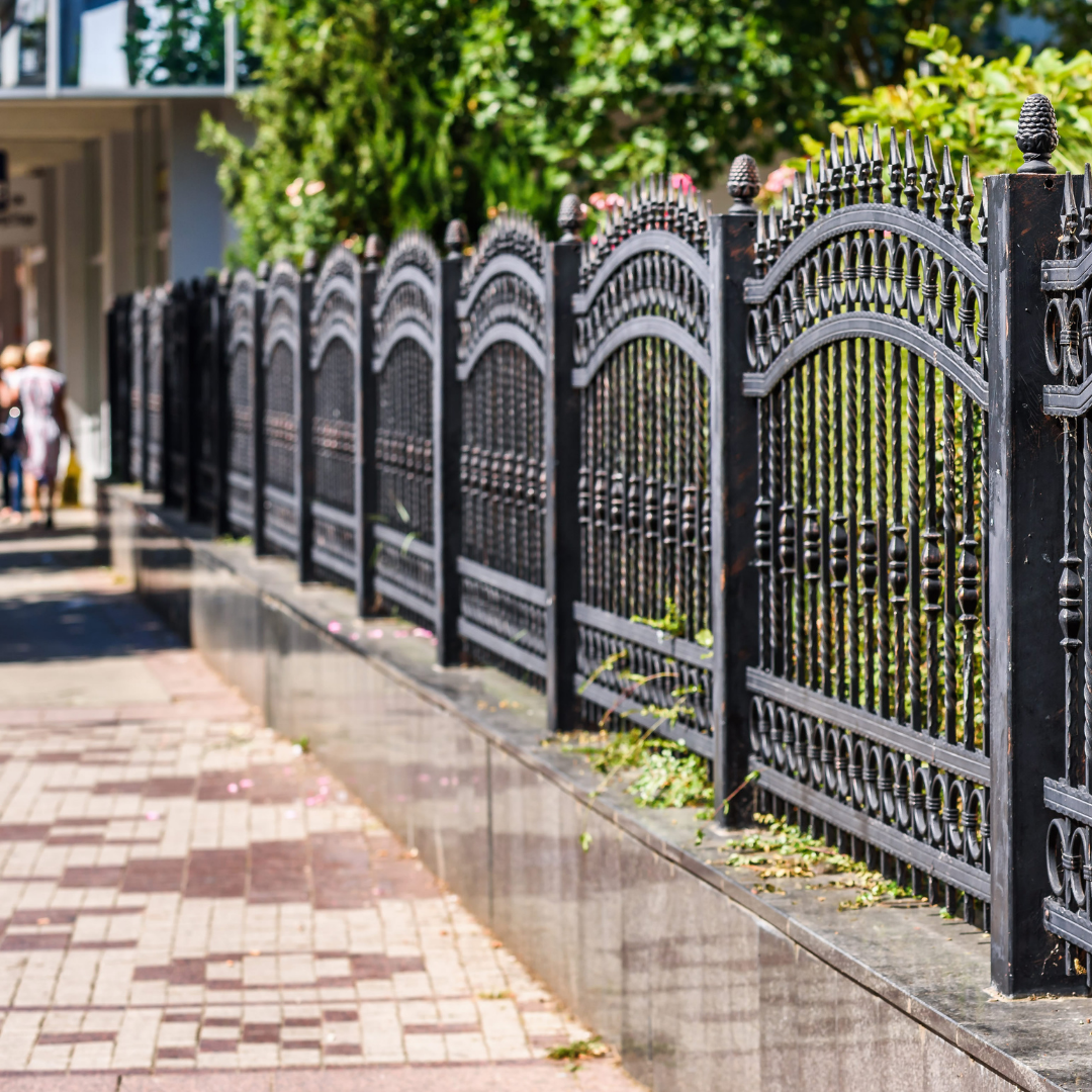 A black wrought iron fence along a sidewalk next to a building.