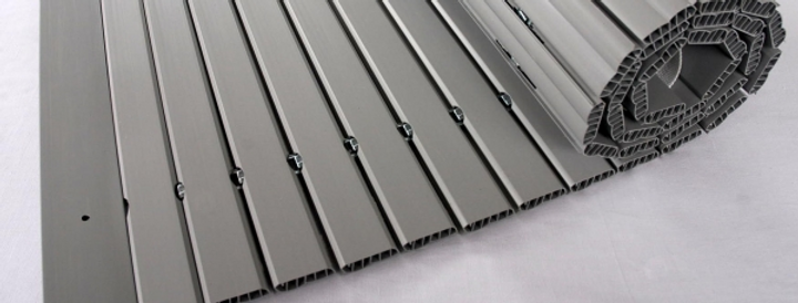 Materiale flessibile, grigio e rigato, arrotolato su uno sfondo bianco.