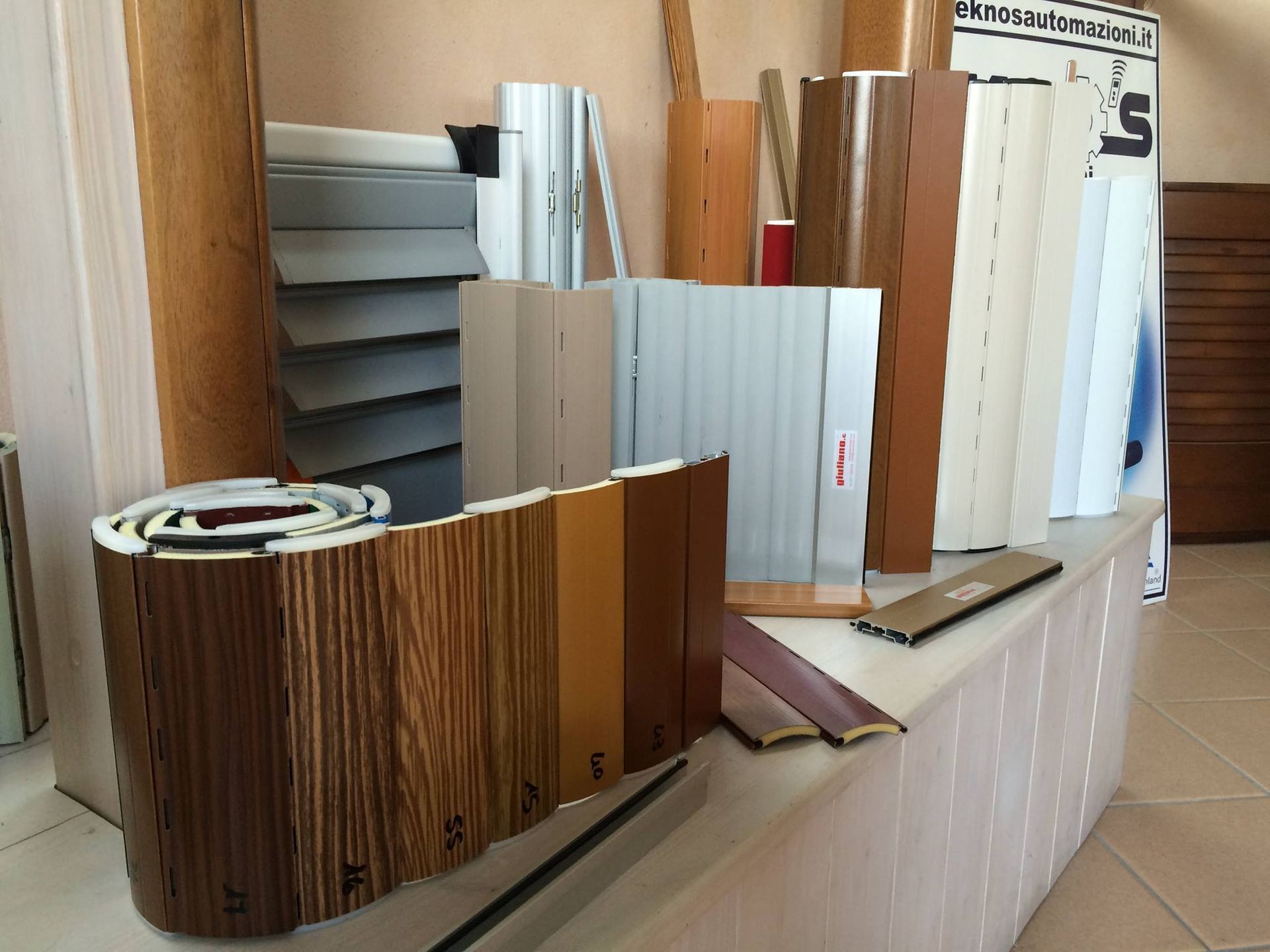 Esposizione di vari materiali da costruzione in legno e di colori neutri, tra cui listelli, su un tavolo espositivo.