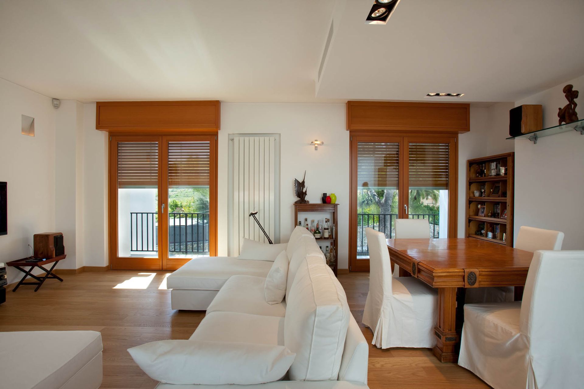 Soggiorno con divano bianco, tavolo da pranzo in legno e due finestre.