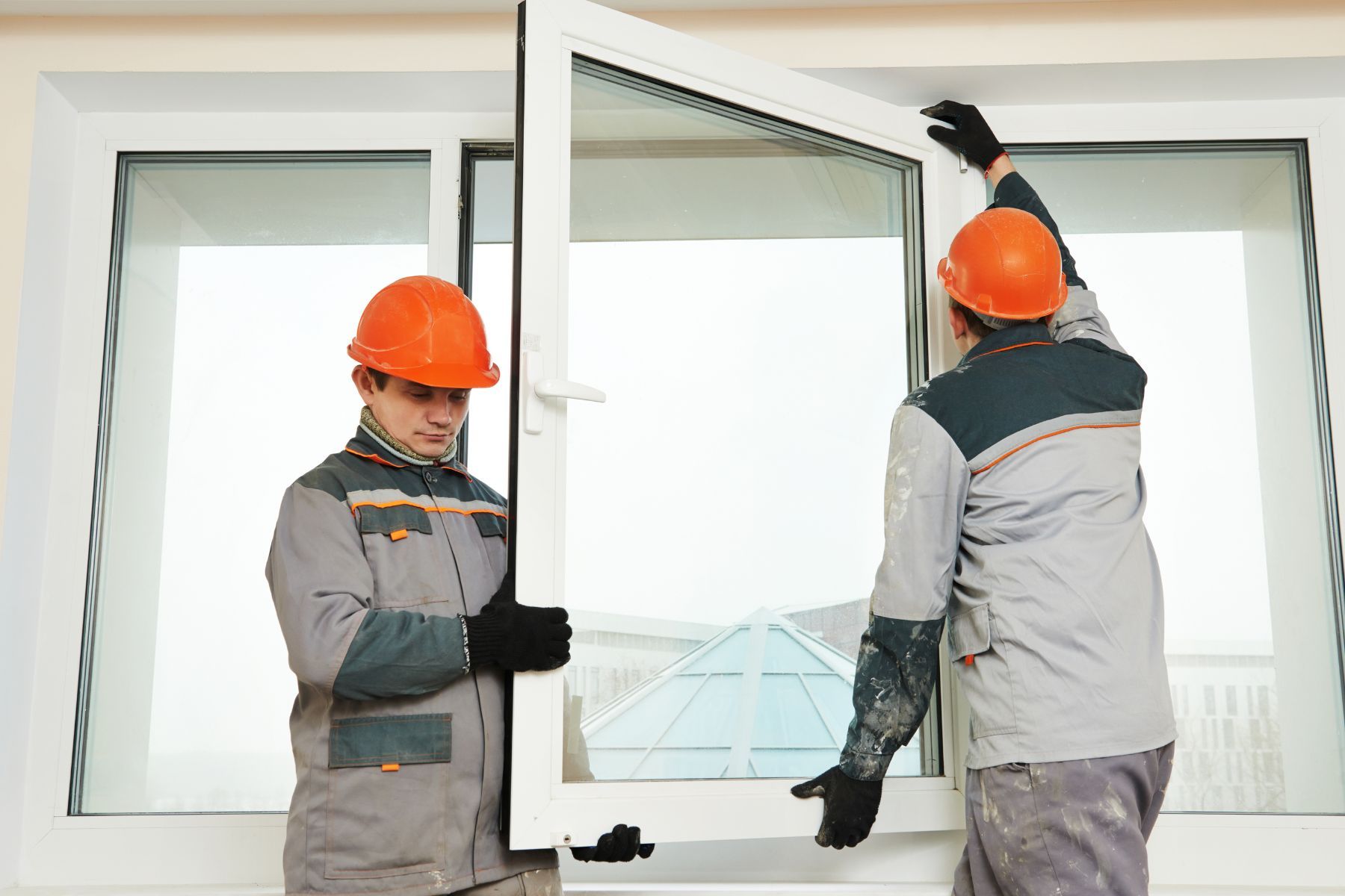 Due operai con il casco stanno installando una finestra bianca in un edificio.