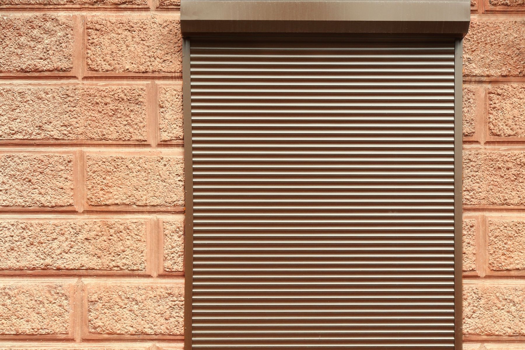 Tapparella marrone che copre una finestra su un muro di mattoni ruvidi.