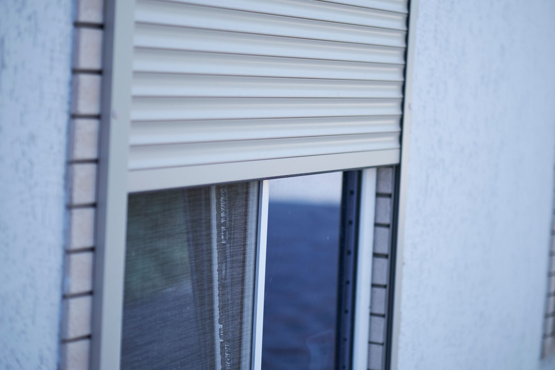 Finestra con tapparella beige parzialmente chiusa sulla facciata esterna di un edificio bianco.