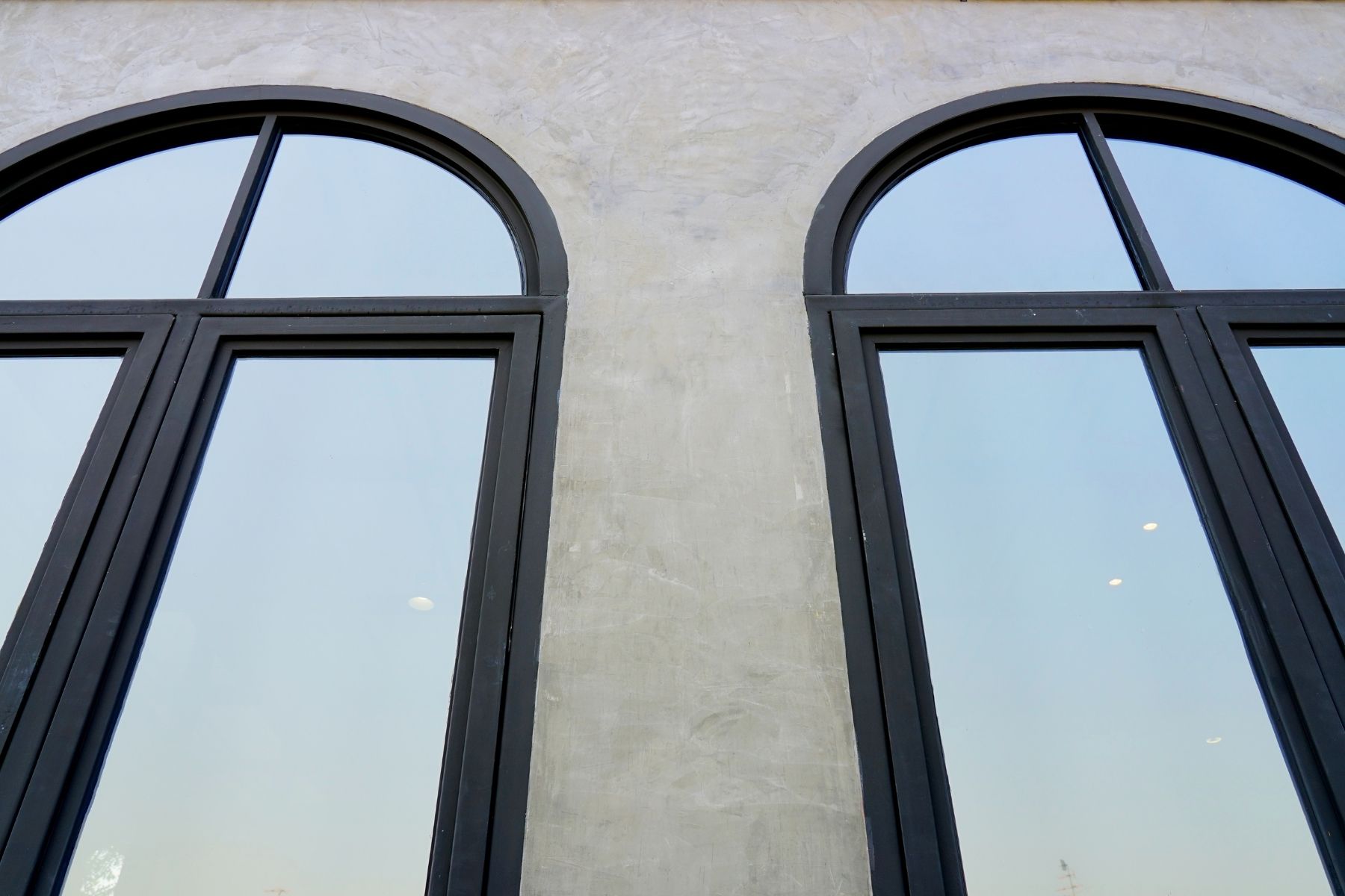 Due finestre ad arco con cornici nere su una parete in stucco grigio.