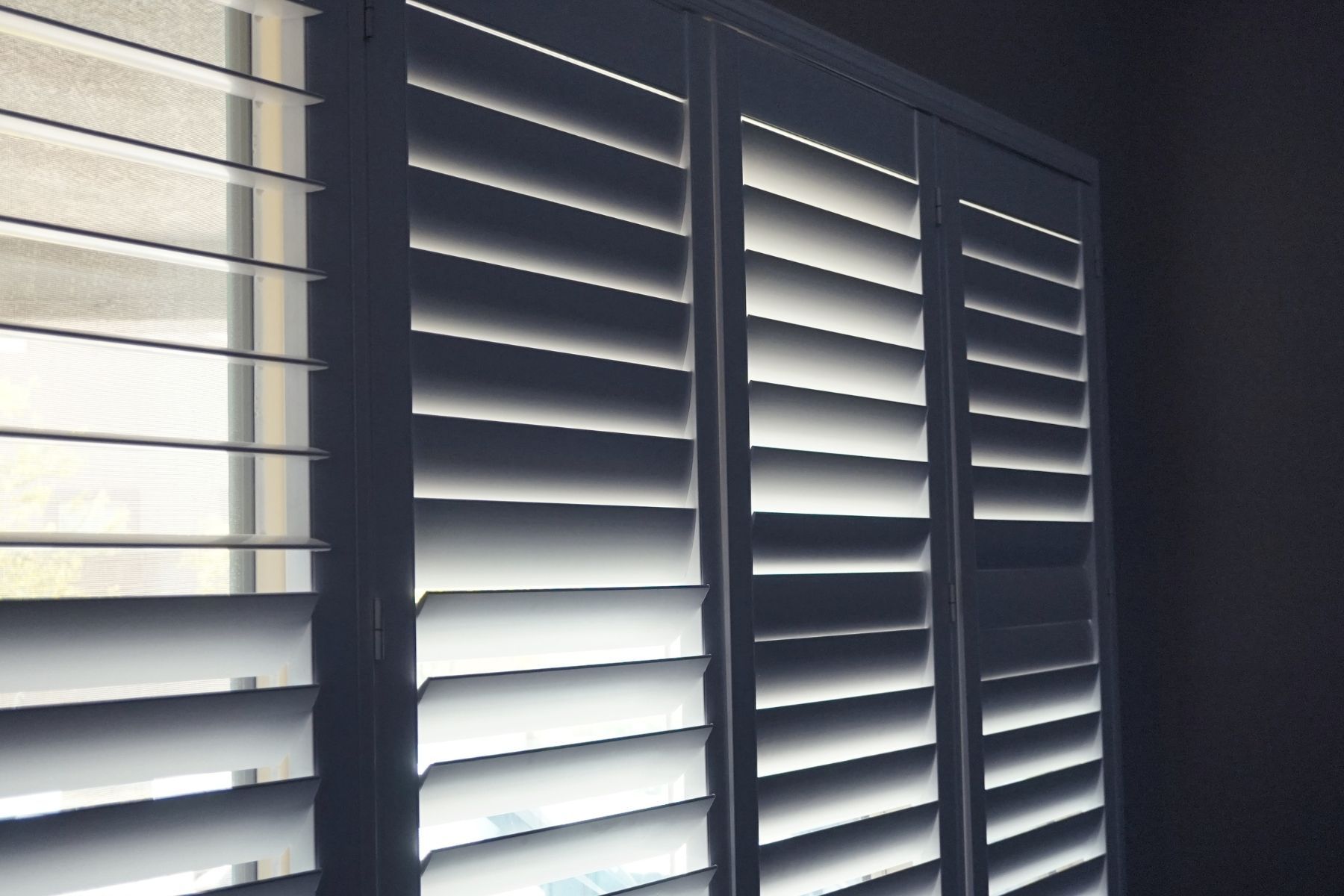 Persiane bianche, con stecche angolate per controllare la luce, all'interno di una stanza.