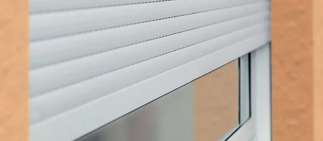 Le tapparelle bianche coprono parzialmente una finestra, vista di sbieco. La parete è di un arancione chiaro.