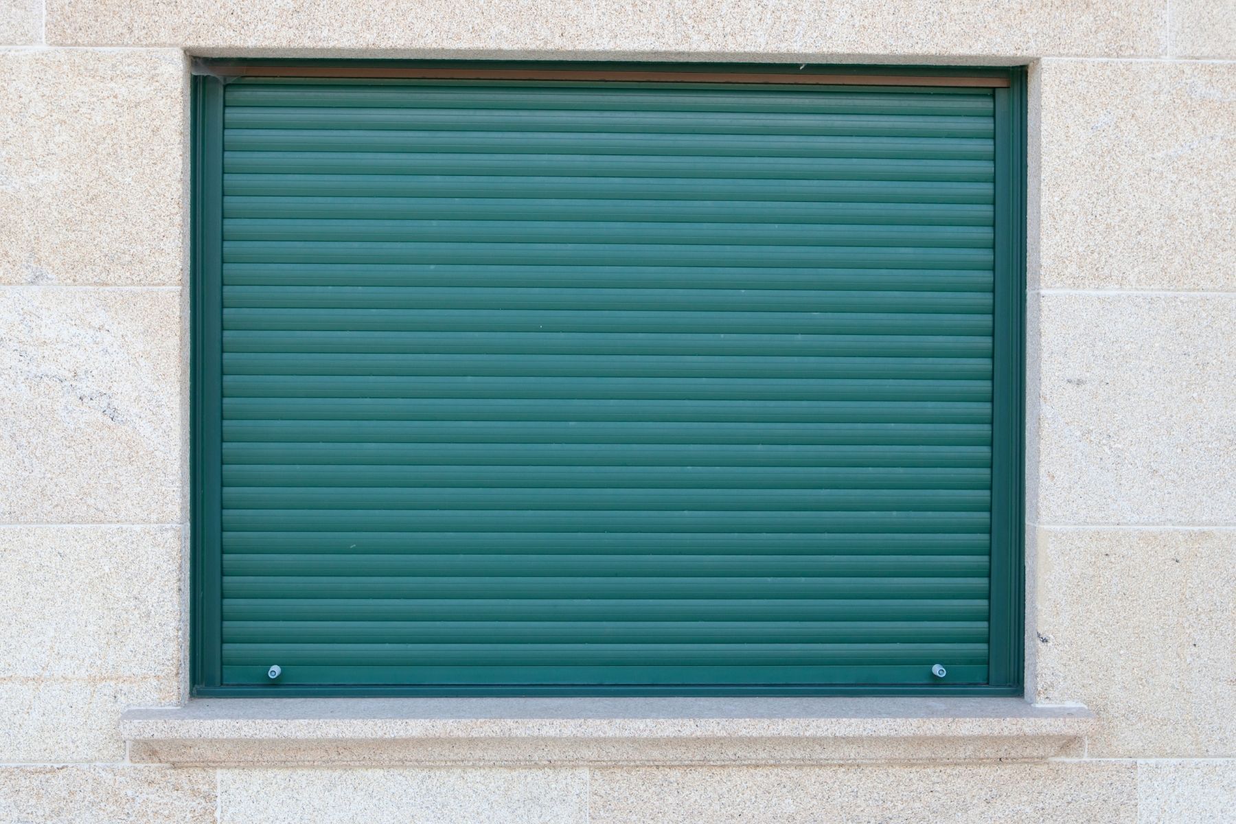 Persiana verde su muro in pietra beige.