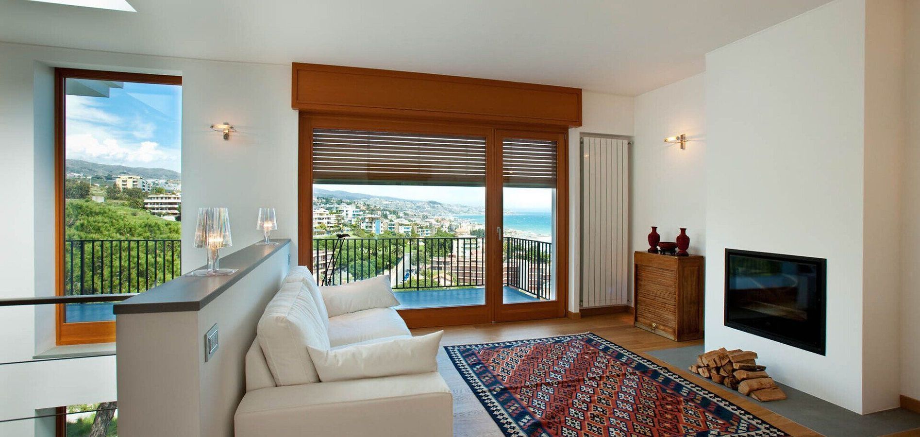 Un soggiorno con divano bianco, camino e ampie finestre che si affacciano su un panorama suggestivo.