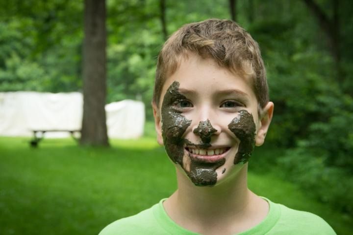 A young boy with mud on his face is smiling.