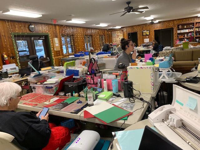 A woman is sitting at a table in a messy room looking at her phone.