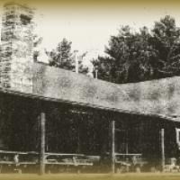 A black and white photo of a pavilion with a chimney and trees in the background.